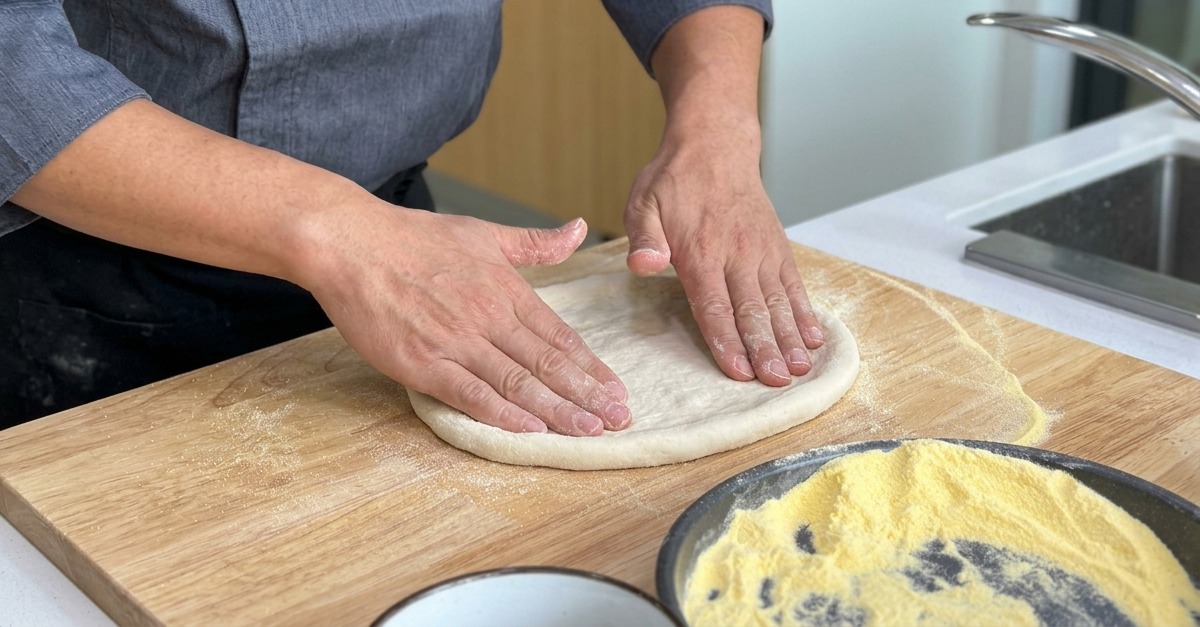Estirando la base de la masa de pizza hacia afuera sobre una tabla de madera, manteniendo un borde elevado más grueso.
