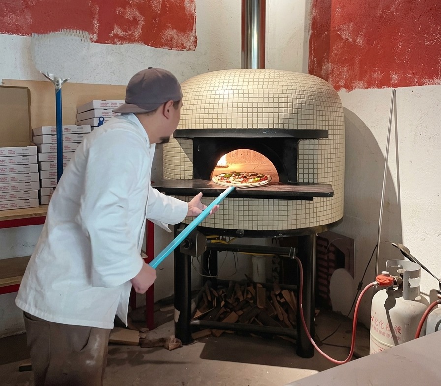 Un chef usando una pala de pizza azul larga para deslizar una pizza cruda en la boca de un horno de ladrillos caliente.