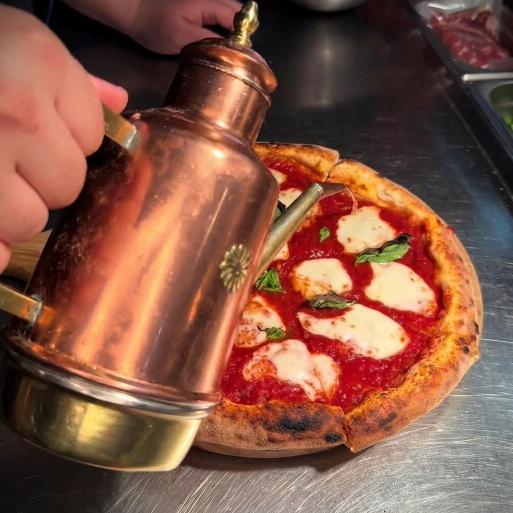 Aceite de oliva dorado siendo rociado desde una aceitera de cobre sobre una pizza Margarita recién cortada.