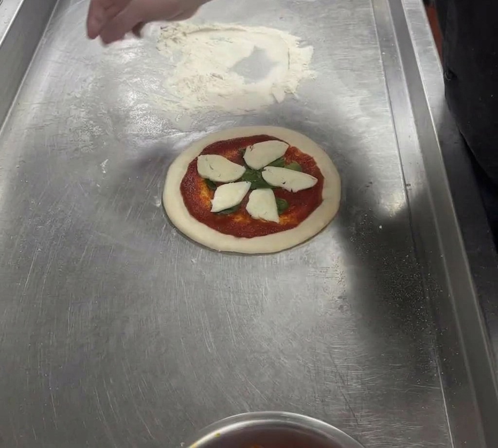 Rodajas de mozzarella blanca dispuestas sobre la masa de pizza con salsa roja.