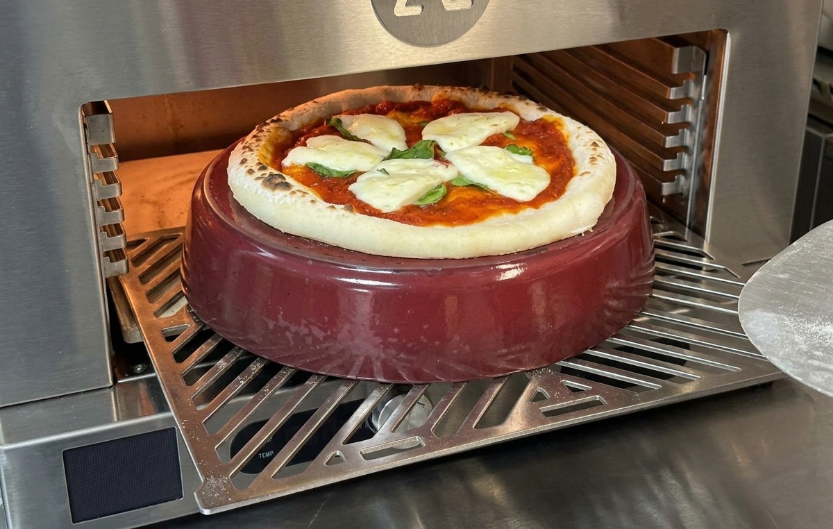 Una pizza parcialmente horneada con mozzarella fundida donde se ve cómo el borde empieza a inflarse.