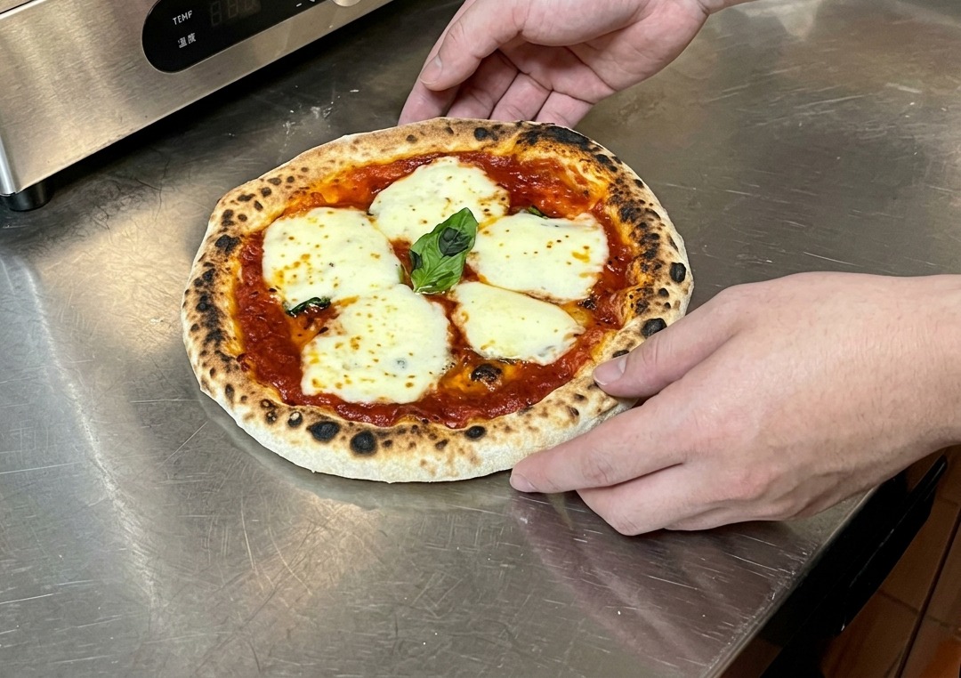 Manos sosteniendo una pizza recién horneada sobre una encimera, preparándose para comprobar la base.