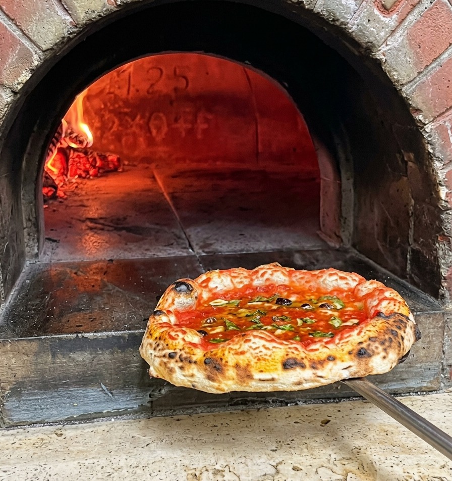 Pizza napolitana recién horneada con bordes tostados saliendo del horno de leña en una pala metálica.