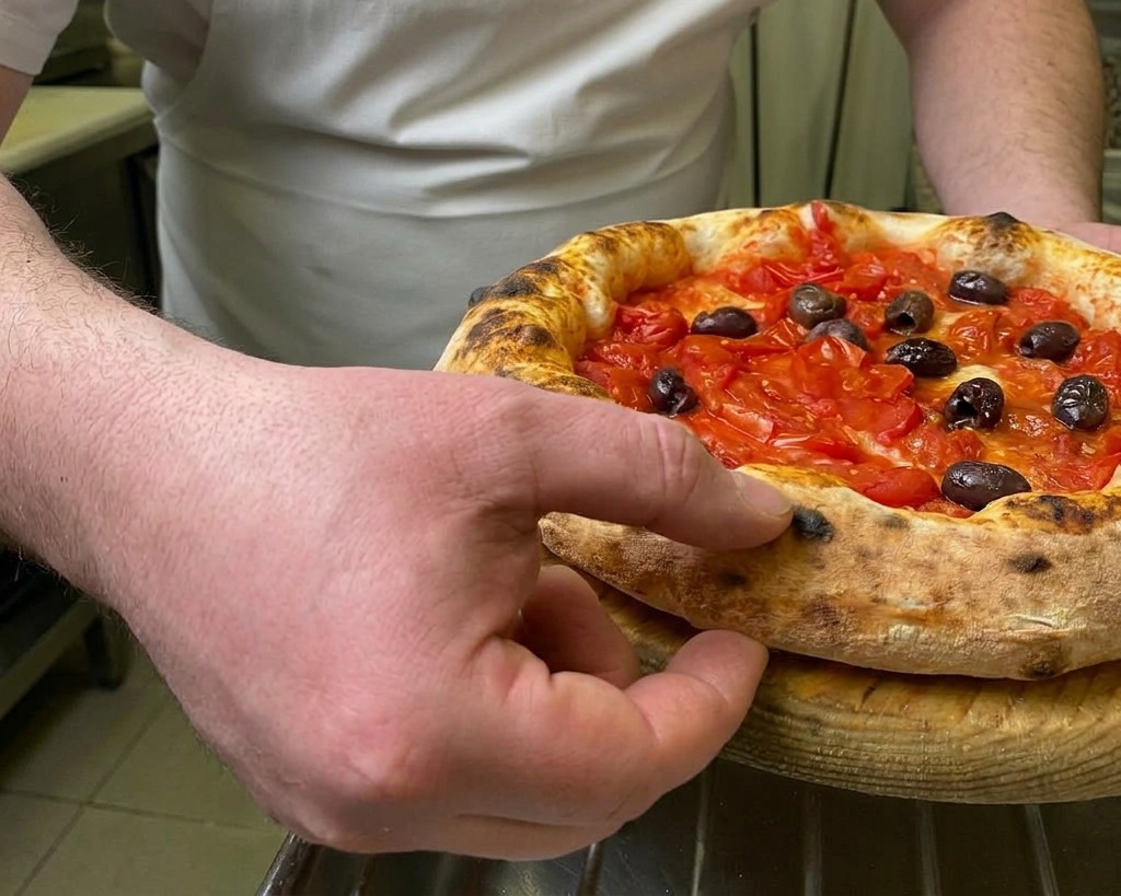 Un chef presionando con el dedo el borde elevado y tostado de una pizza recién horneada para probar su textura elástica.