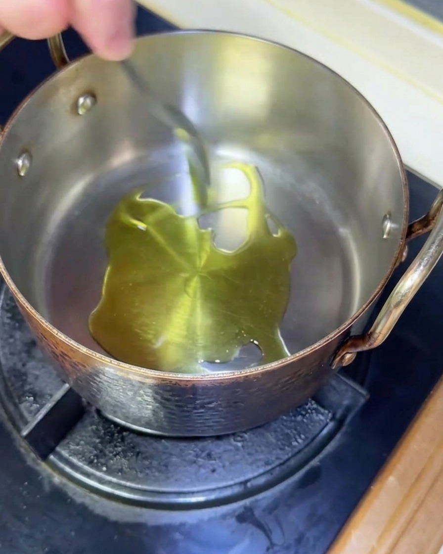 Aceite de oliva brillando mientras se calienta en una olla de cobre sobre un fogón de gas.
