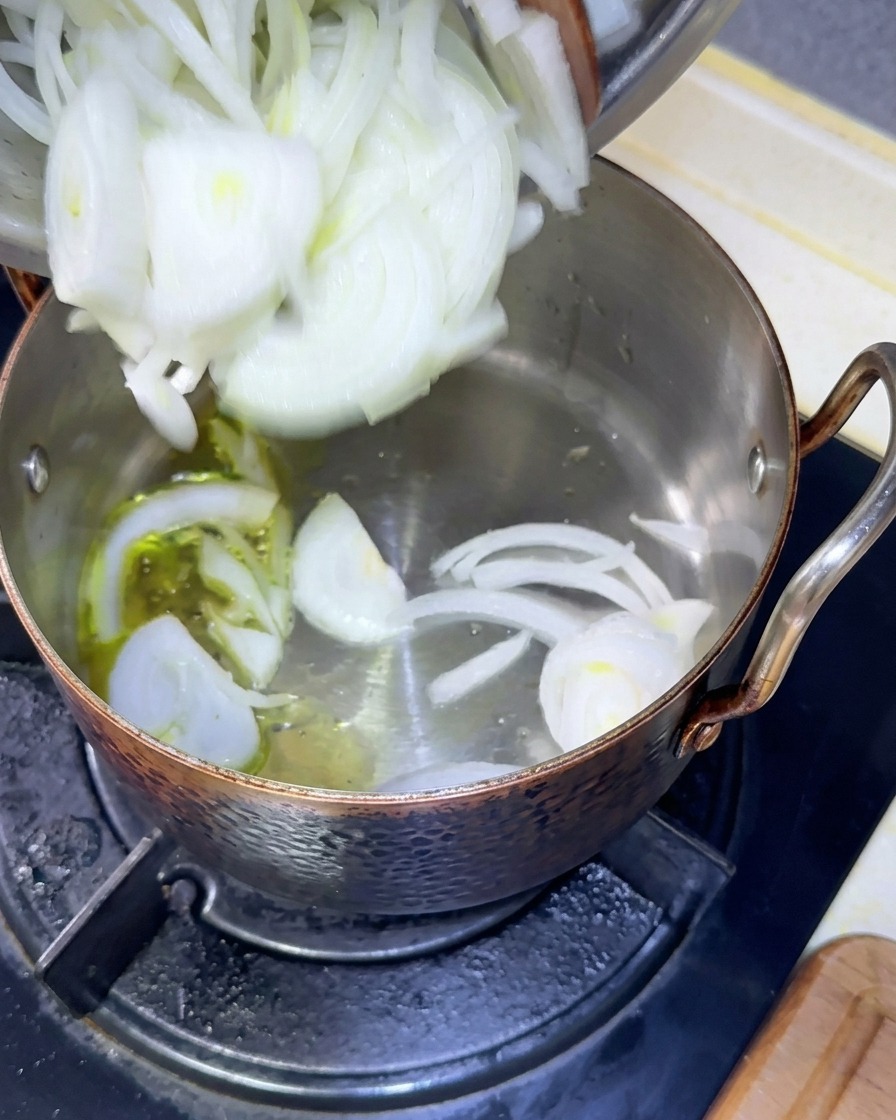 Cebollas blancas recién cortadas vertiéndose desde un bol a una olla con aceite de oliva caliente.
