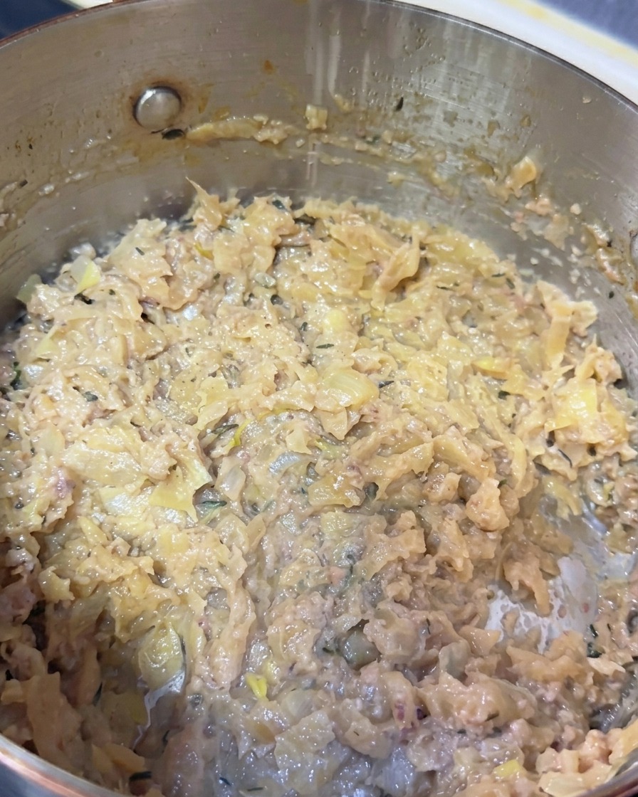 Primer plano del interior de una olla con cebollas caramelizadas, pasta de pescado y restos de tomillo.