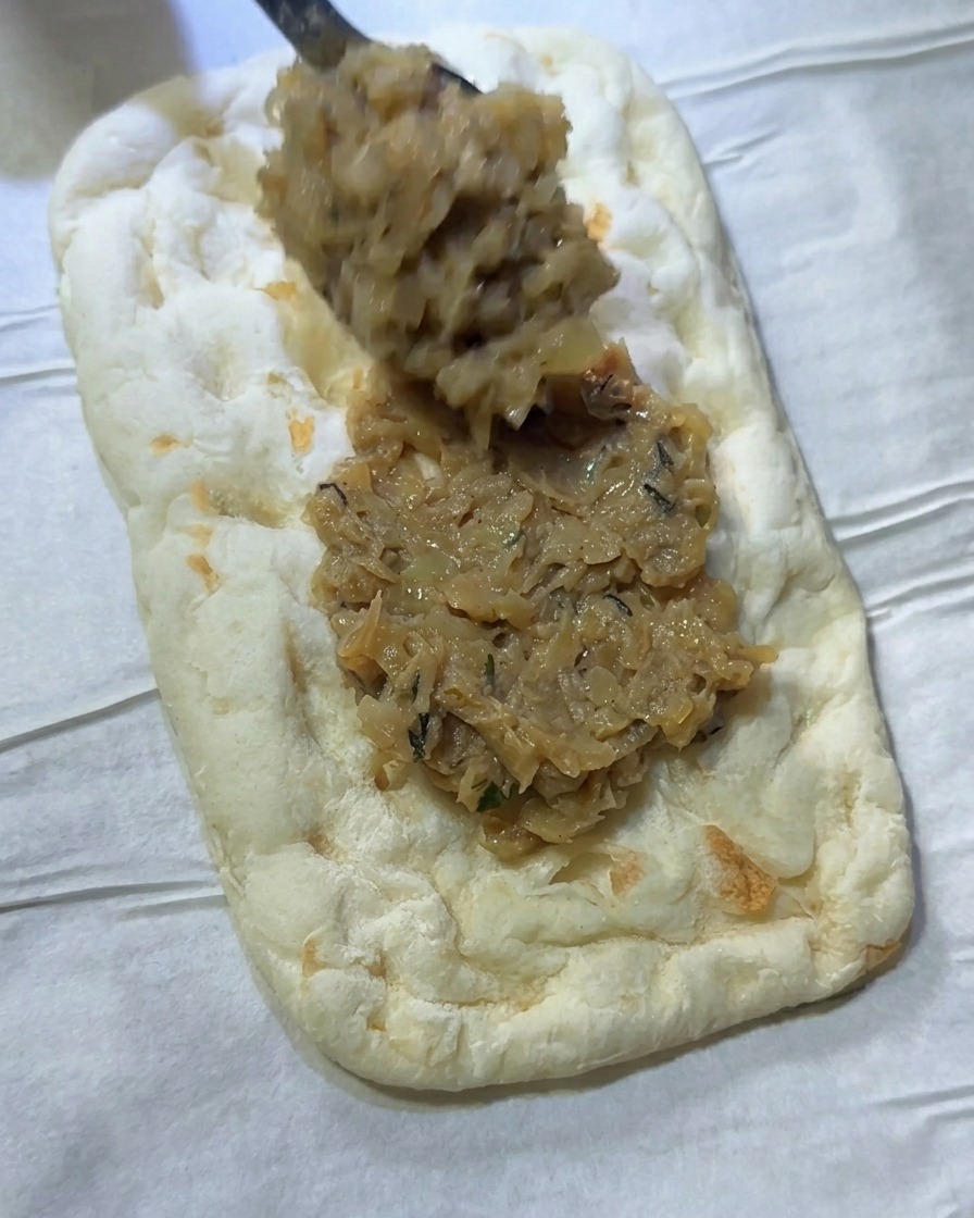 Una cucharada de la mezcla de cebolla extendiéndose uniformemente sobre una masa rectangular.