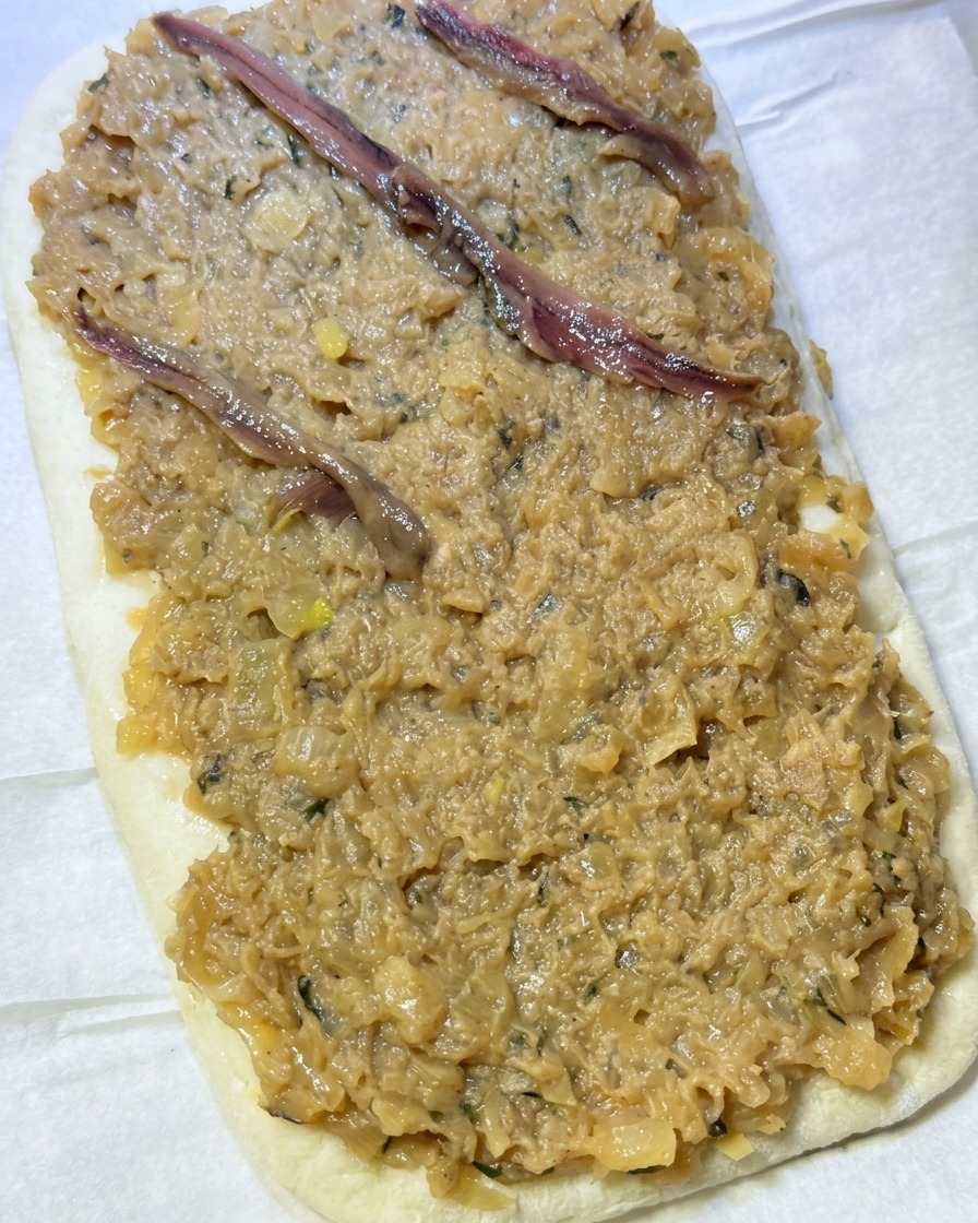 Filetes de anchoa colocándose en un patrón de diamante sobre la capa de cebolla en la masa.