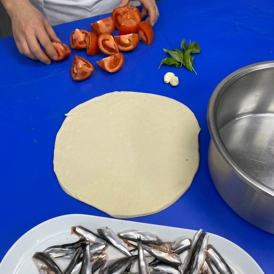 Manos de un chef recogiendo tomates en cuartos, ajo y albahaca fresca para la salsa.