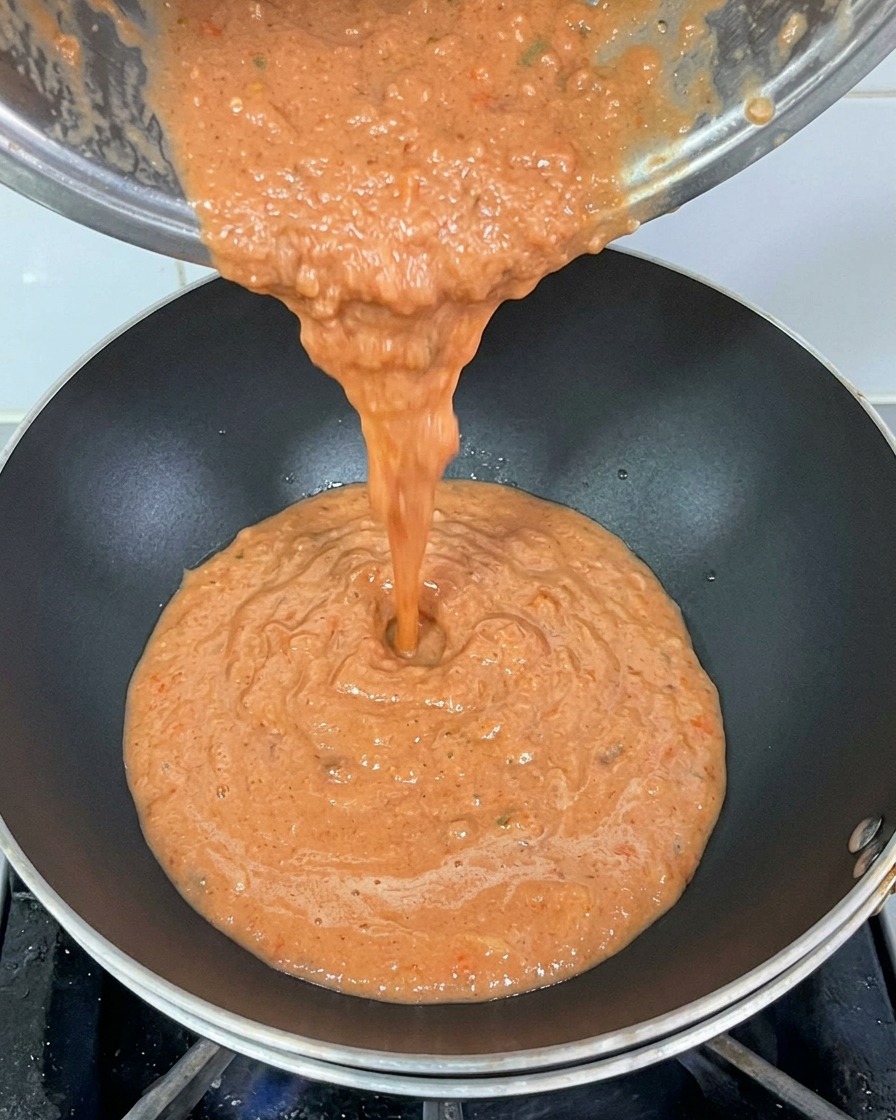 Vertiendo la espesa salsa de tomate roja desde una olla de metal a un wok caliente.