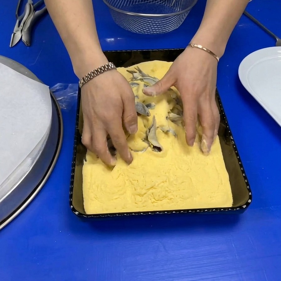 Manos de un chef mezclando boquerones enteros en una bandeja con harina de maíz amarilla.