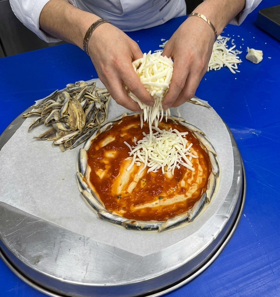 Manos esparciendo generosamente queso rallado sobre la salsa de tomate de la pizza.