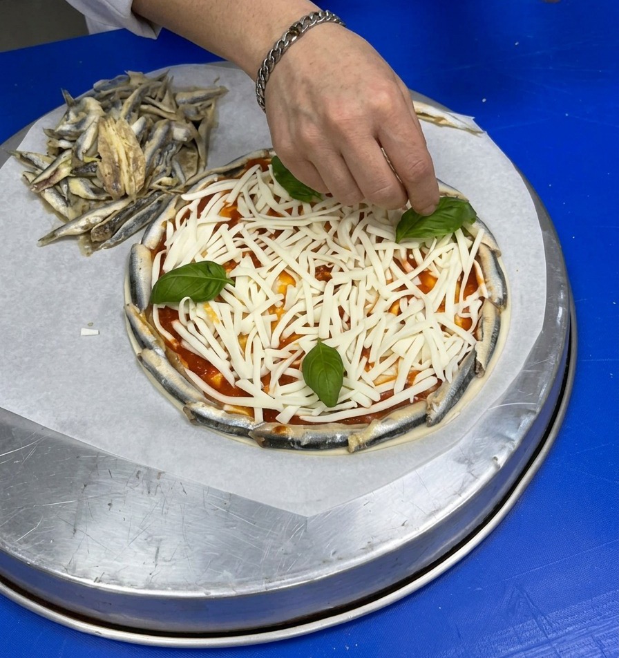 Una mano colocando hojas enteras de albahaca fresca sobre el queso rallado en la pizza.