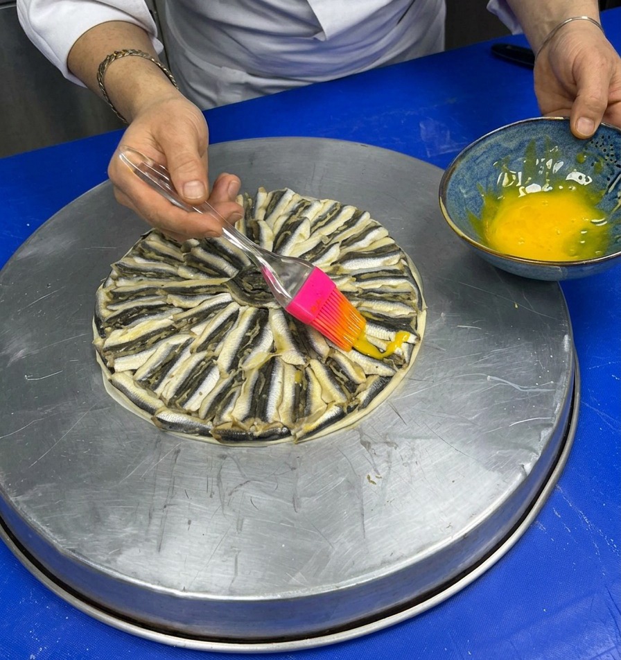 Uso de un pincel de silicona para pintar con huevo batido la parte superior de la pizza de boquerones.