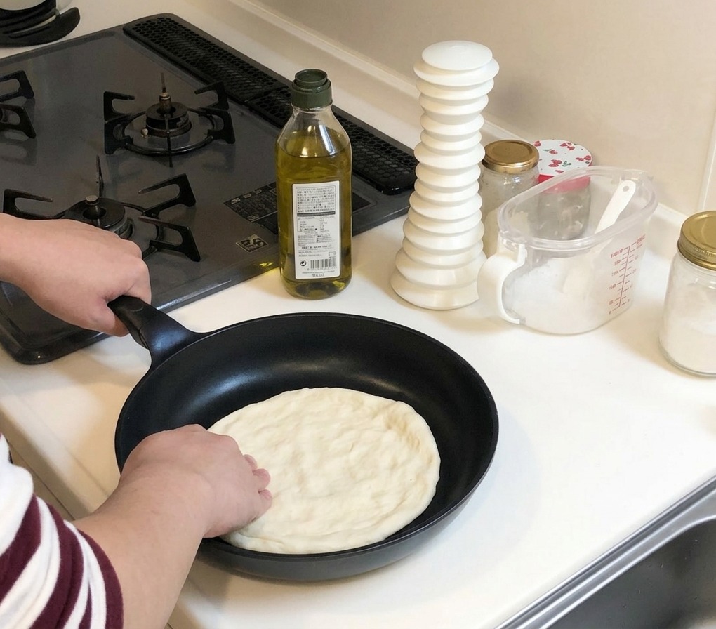 Manos presionando y estirando un trozo de masa cruda de pizza hacia los bordes de una sartén negra fría.