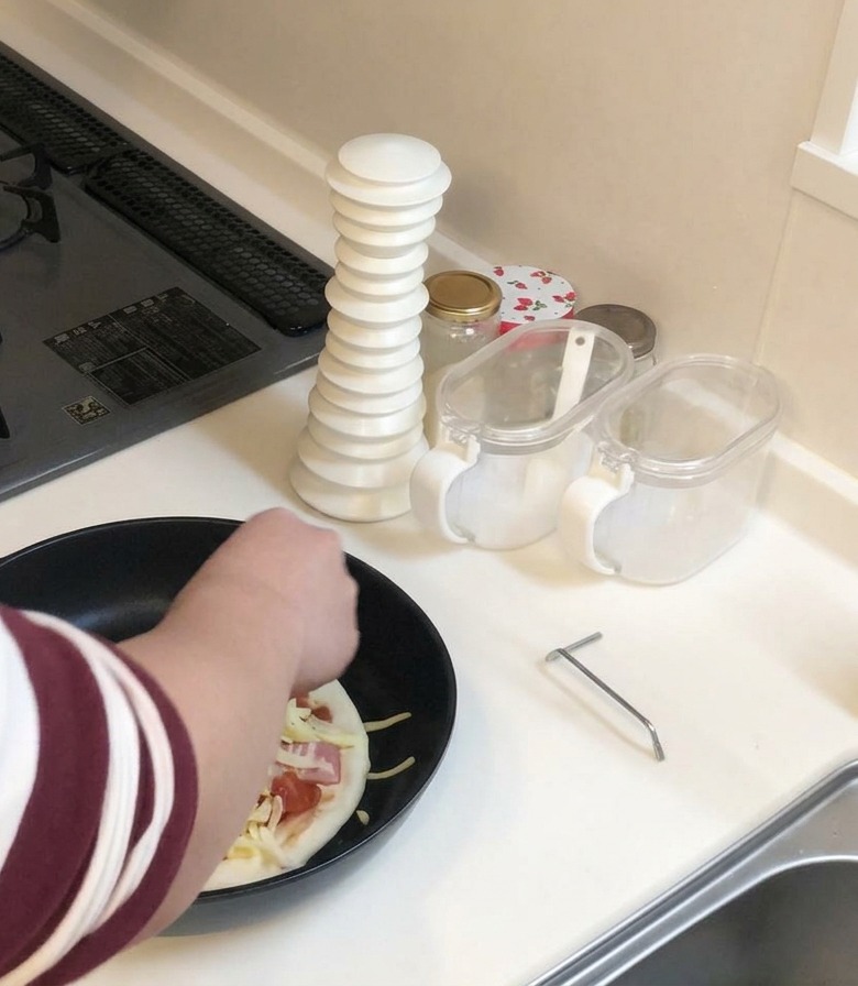 Una persona con camisa a rayas añadiendo un puñado generoso de queso rallado sobre la pizza en la sartén.