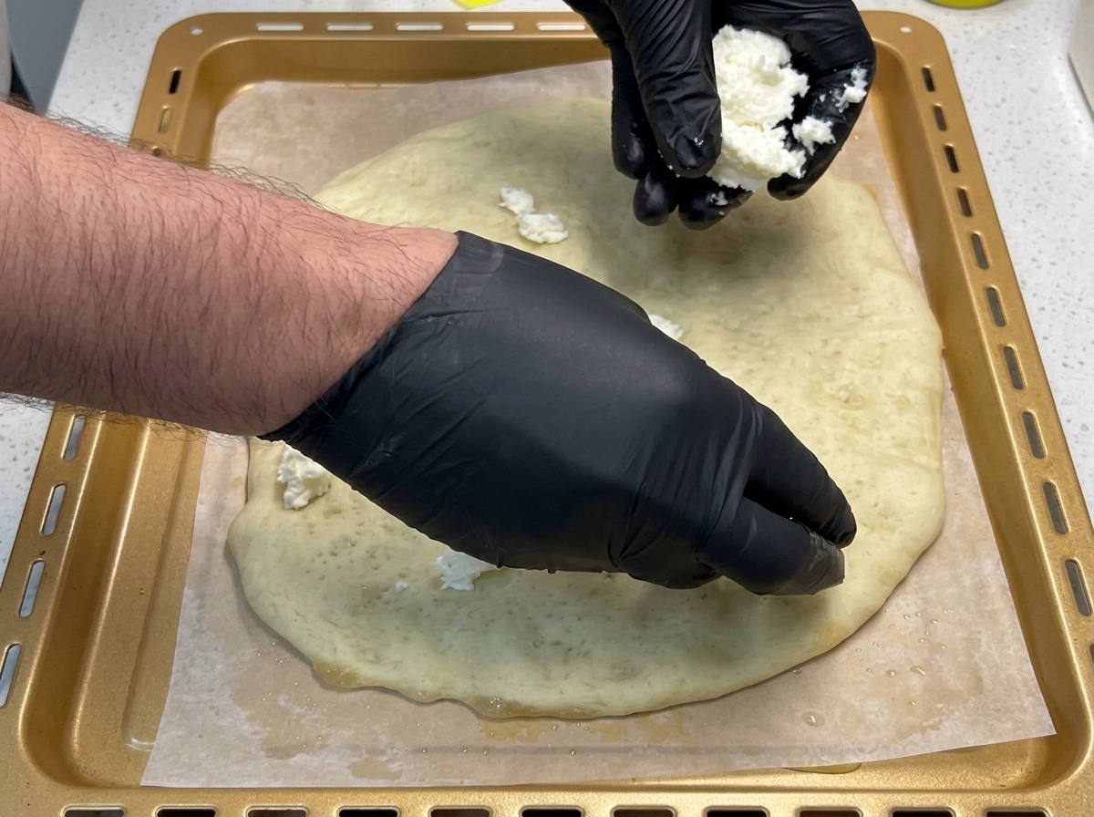 Manos colocando trozos de mozzarella fresca sobre la masa de pizza pre-horneada.