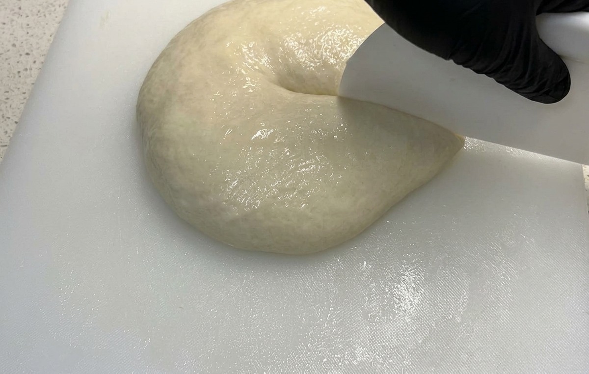 Una rasqueta blanca presionando sobre una masa de pizza esponjosa para dividirla por la mitad.