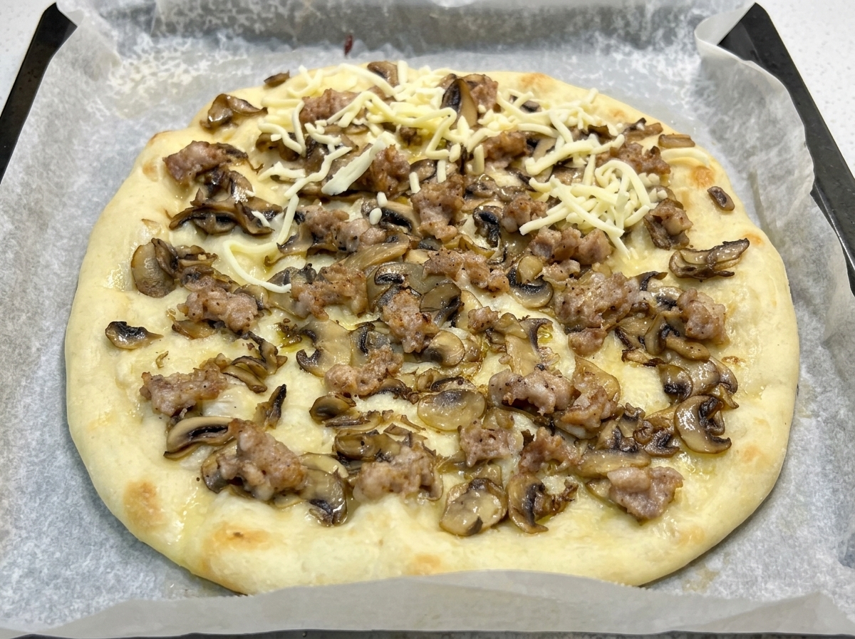 Una base de pizza precocinada con champiñones y salchicha cubierta con una generosa capa de mozzarella rallada.
