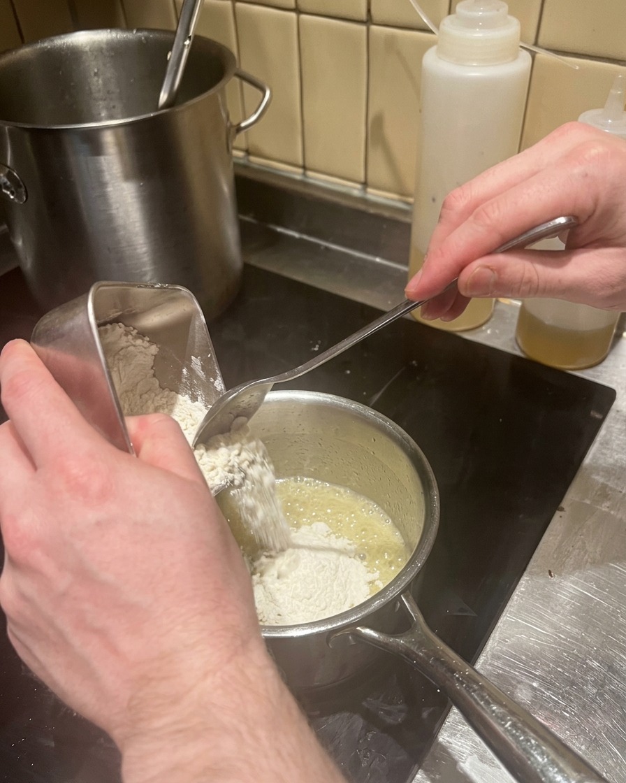 Añadiendo harina a la mantequilla derretida para hacer un roux.