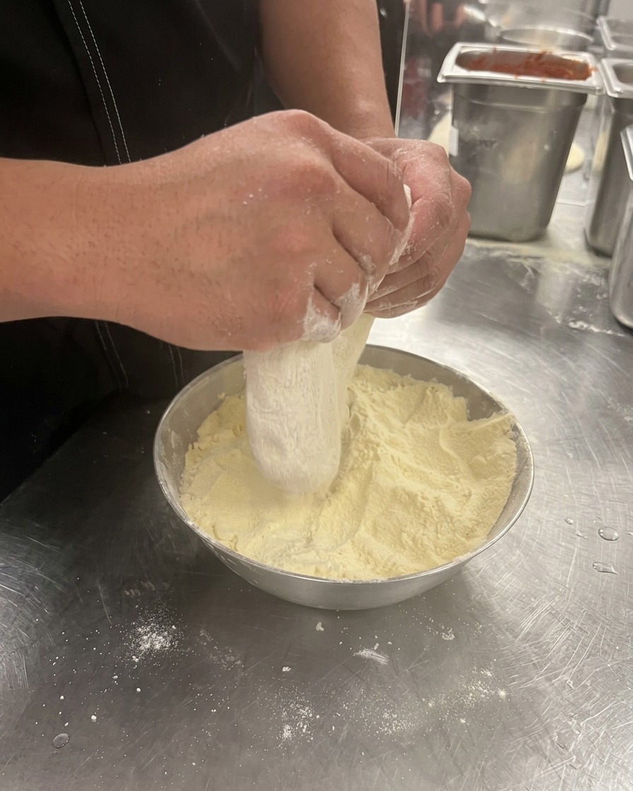 Manos presionando y estirando una bola de masa de pizza en un bol con harina.