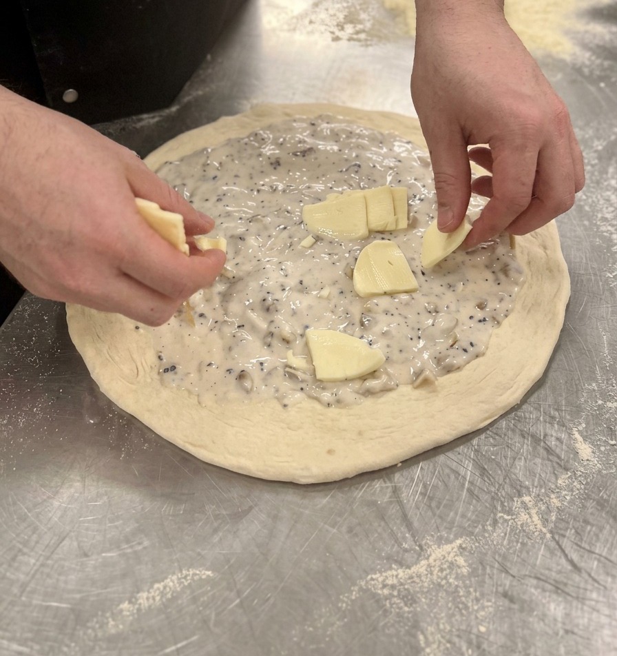 Manos colocando trozos de mozzarella uniformemente sobre la salsa blanca en la pizza cruda.