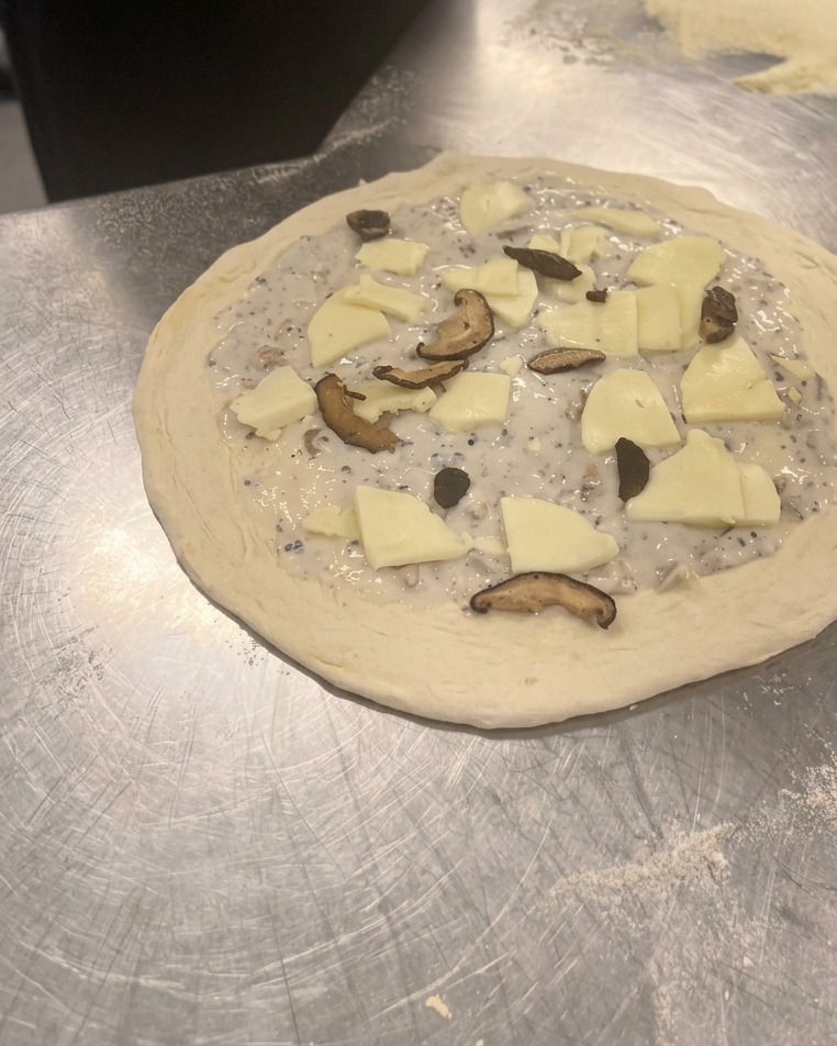 Esparciendo láminas de shiitake y champiñones cocinados sobre el queso en la pizza cruda.
