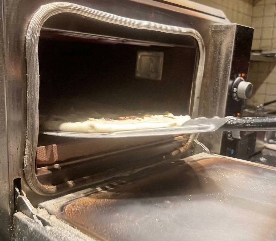 Pizza de champiñones cruda siendo introducida en un horno de pizza caliente con una pala de metal.
