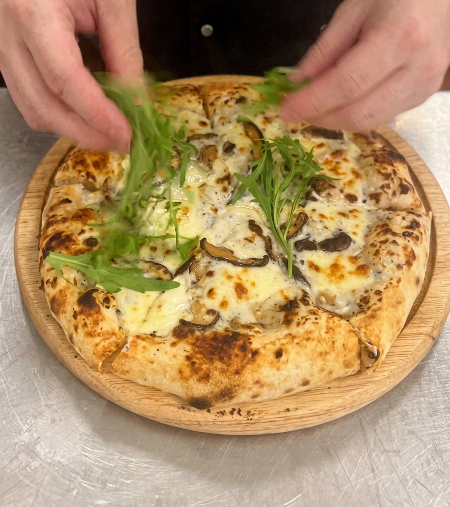 Manos colocando hojas verdes de rúcula sobre una pizza de champiñones ya horneada y cortada.