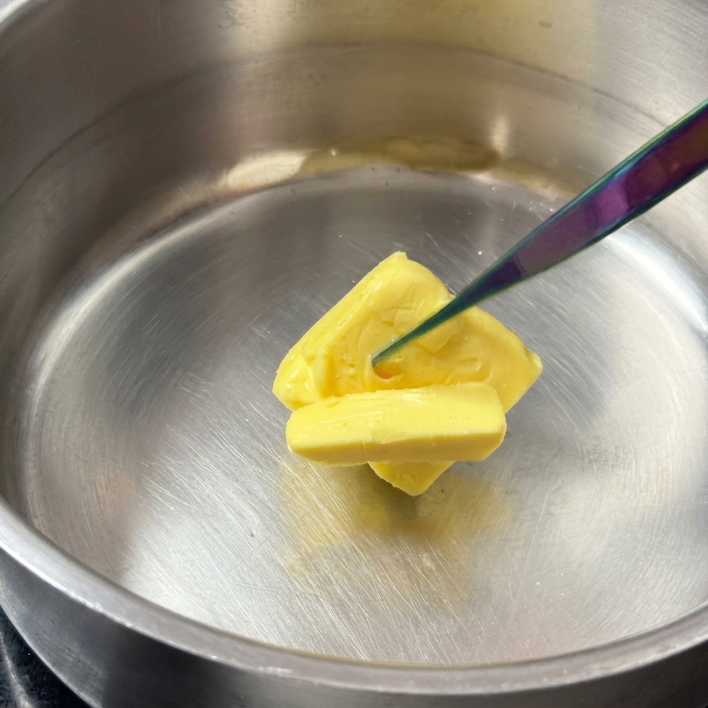 Un bloque de mantequilla amarilla derritiéndose en una olla de acero inoxidable.