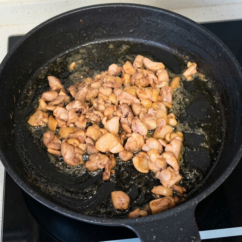 Trozos de pollo cocinados y dorados salteándose en una sartén negra.
