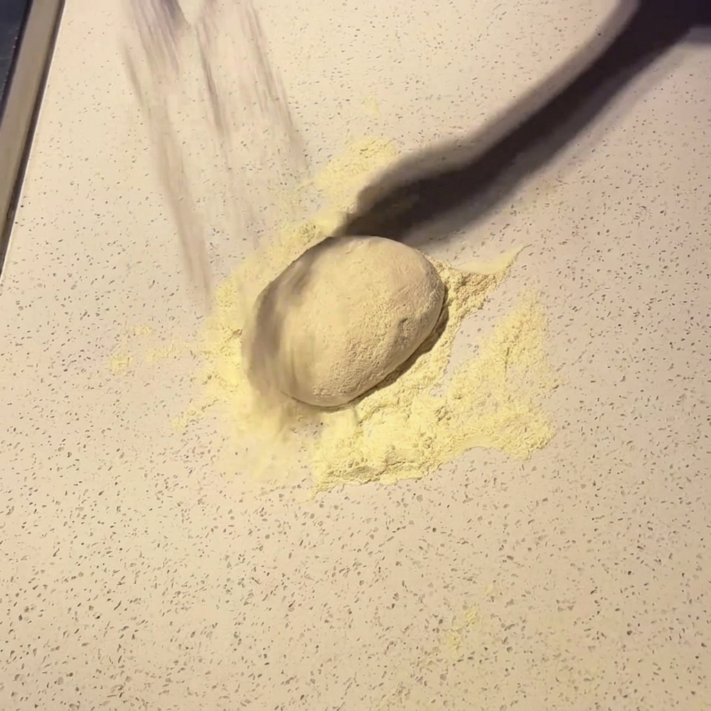 Una bola de masa para pizza espolvoreada con harina sobre una encimera clara.