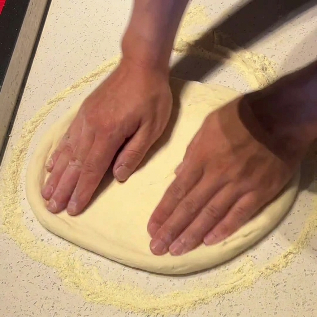 Manos estirando y rotando la masa de pizza sobre una superficie con harina.