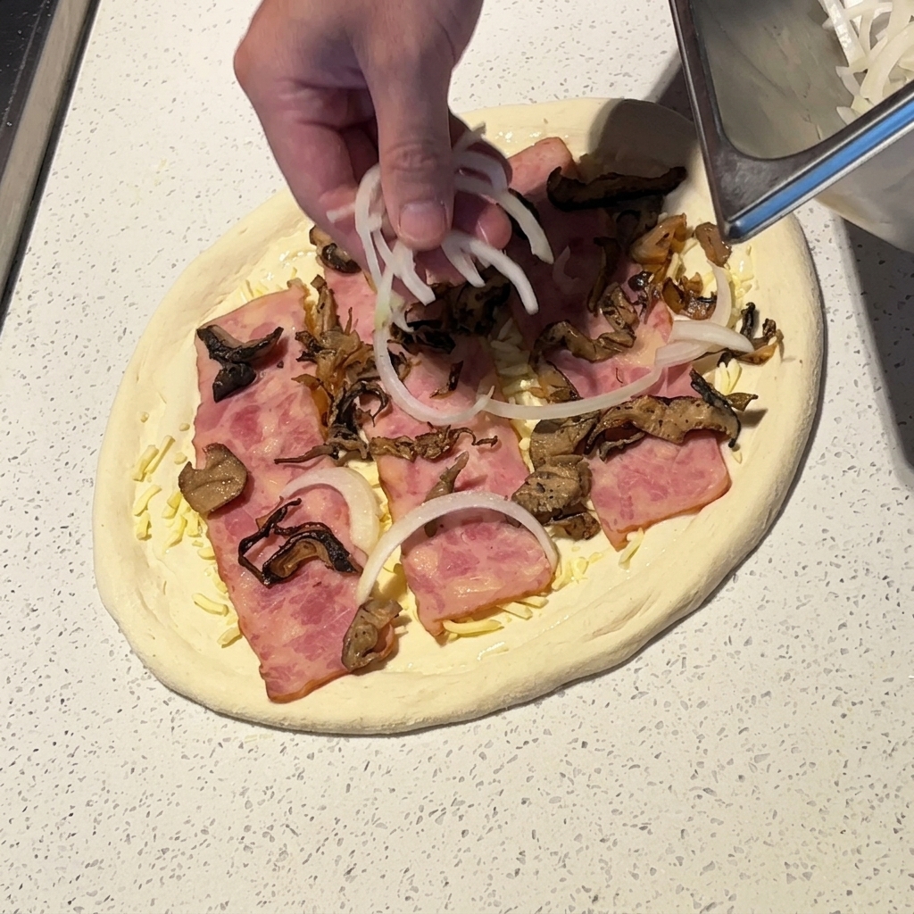 Una mano esparciendo láminas finas de cebolla blanca sobre la pizza preparada.