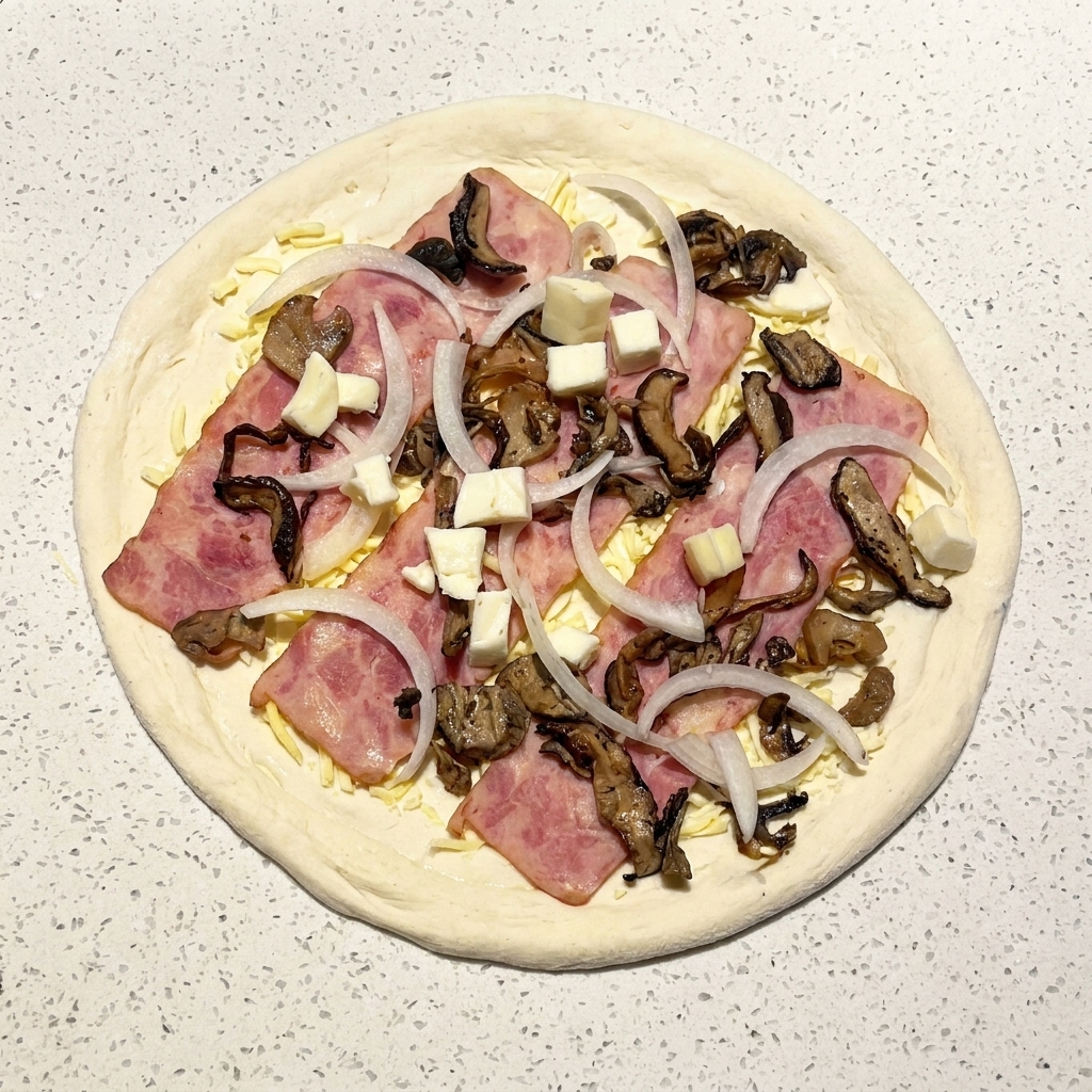 Pizza cruda montada con bacon, champiñones, cebolla y cubos de mozzarella fresca.
