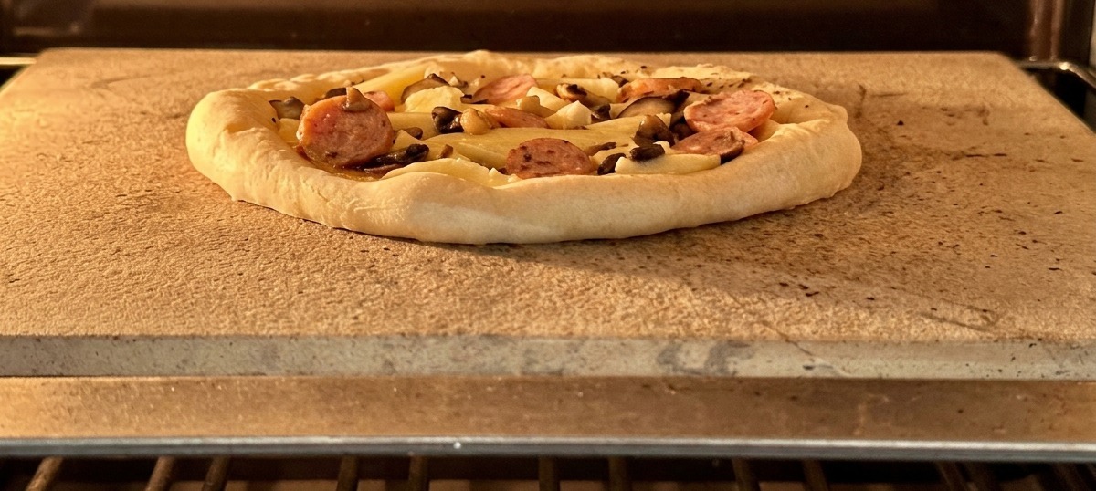 Pizza con salchicha y champiñones lista para entrar al horno sobre una piedra caliente.