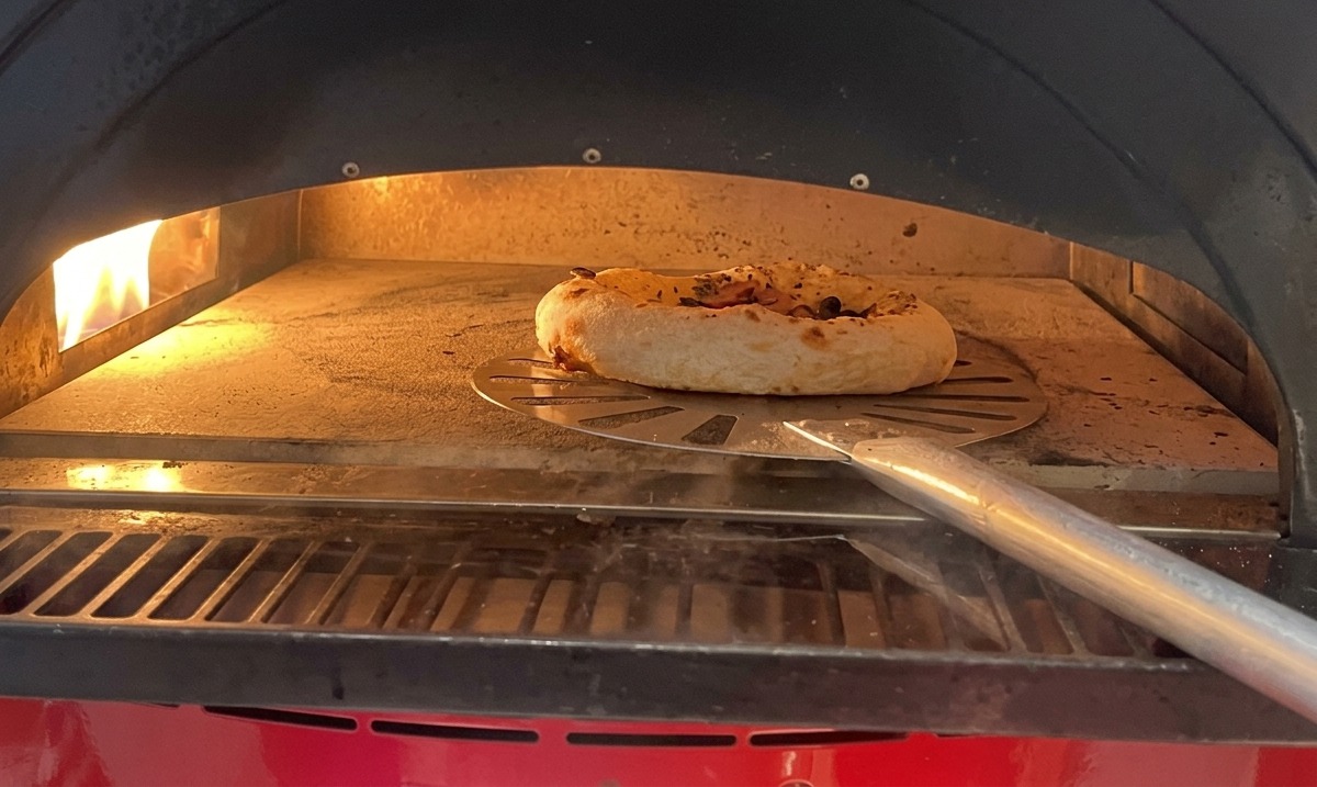 Pequeña pizza horneándose sobre piedra, con el borde visiblemente inflado y manchas doradas.
