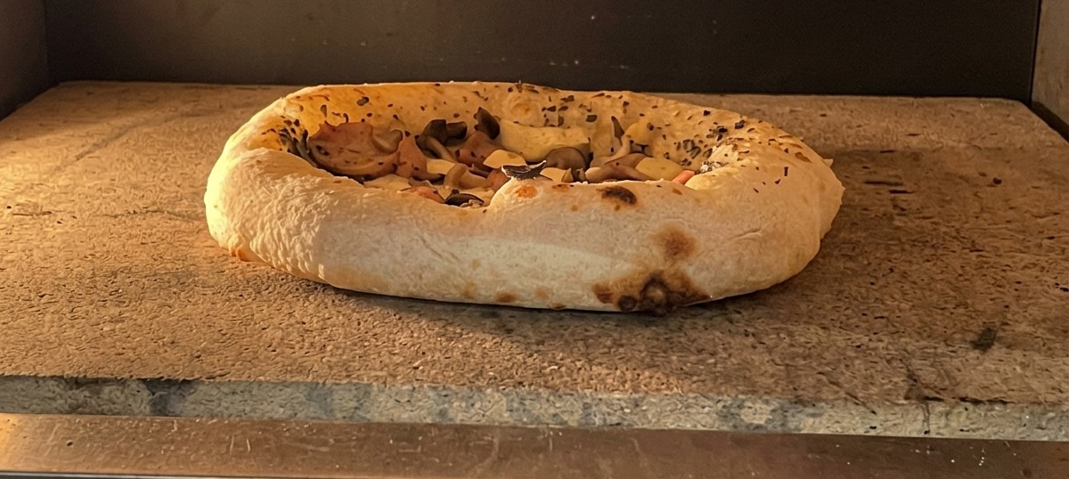 Pizza recién sacada del horno con el borde tostado y el queso burbujeando.