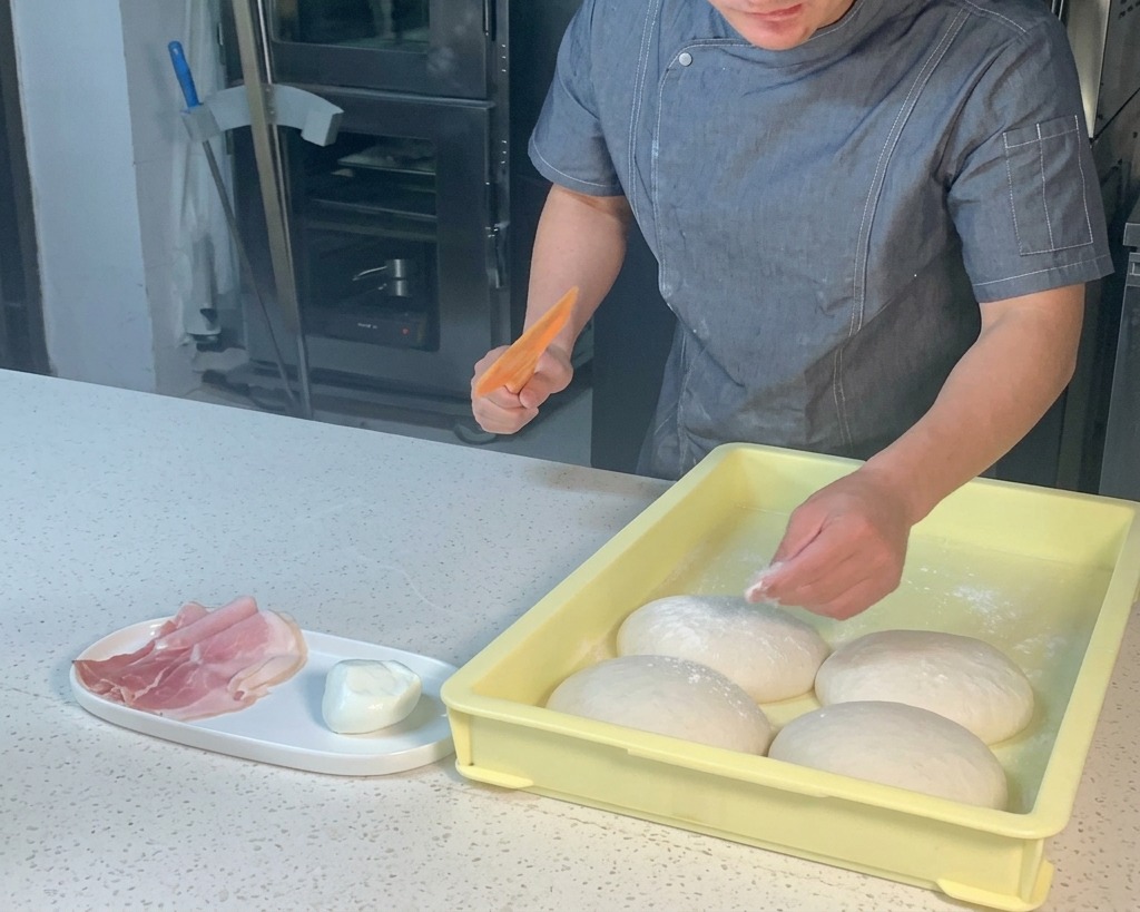 Cocinero usando una espátula de plástico naranja para levantar una bola de masa de una bandeja amarilla.