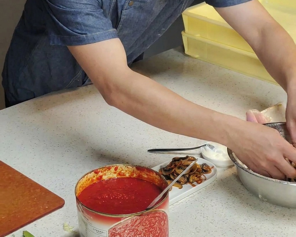 Manos de un cocinero sumergiendo la masa de pizza fermentada en un cuenco con harina blanca.