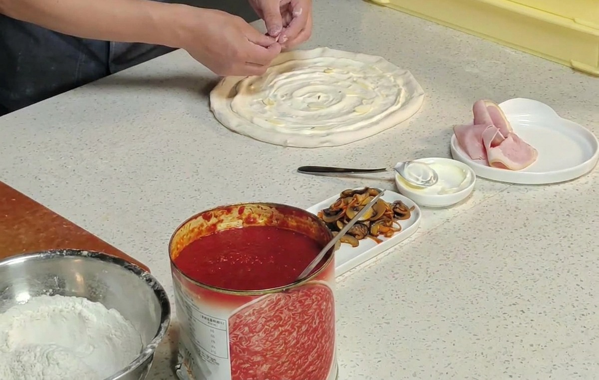 Manos colocando flores de cordyceps naranjas sobre la pizza con salsa blanca.
