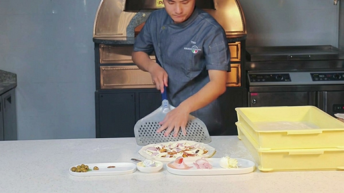 Cocinero frotando harina sobre una pala de metal perforada.
