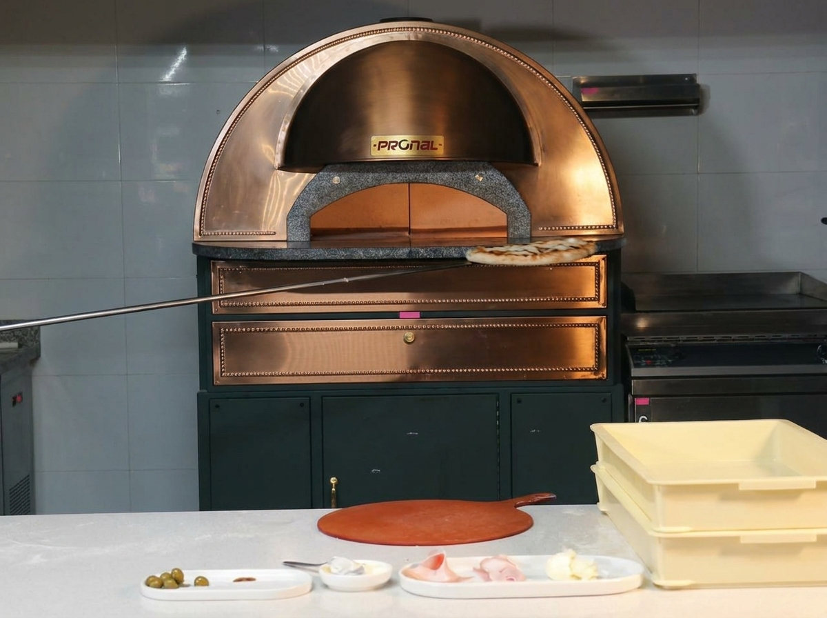 Pizza perfectamente horneada saliendo de un horno de cobre sobre una pala de metal.