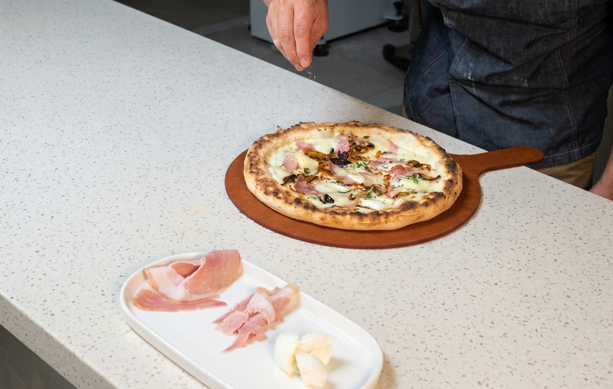 Mano espolvoreando queso rallado sobre la pizza recién sacada del horno.