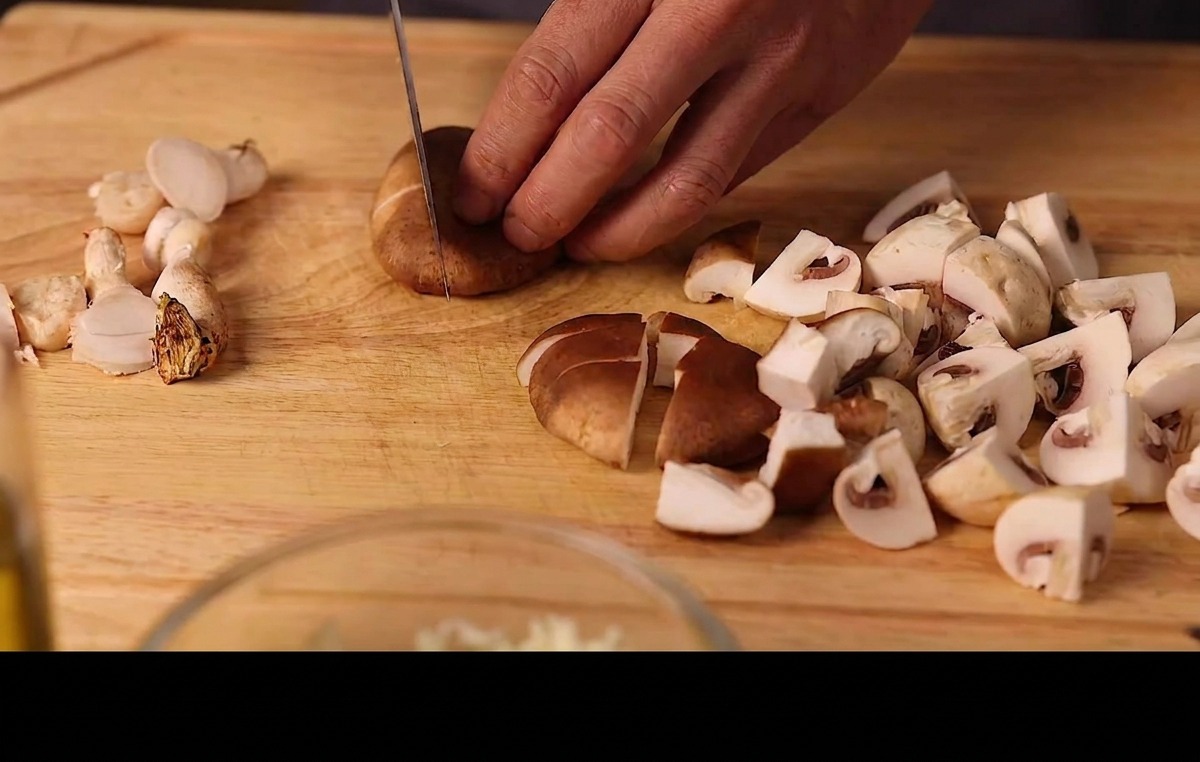 Manos cortando champiñones y setas shiitake frescas en láminas sobre una tabla de madera.