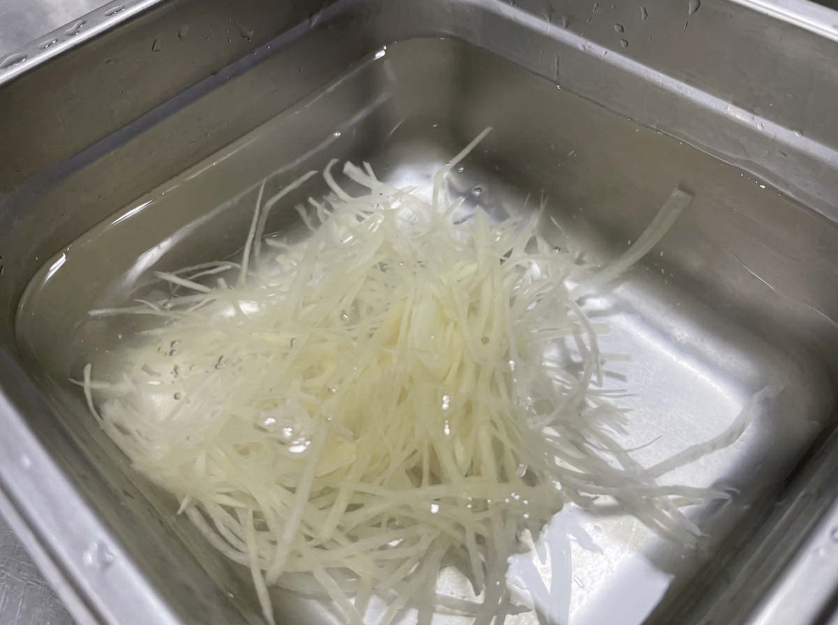 Tiras de papa en juliana sumergidas en un recipiente de acero inoxidable con agua limpia.