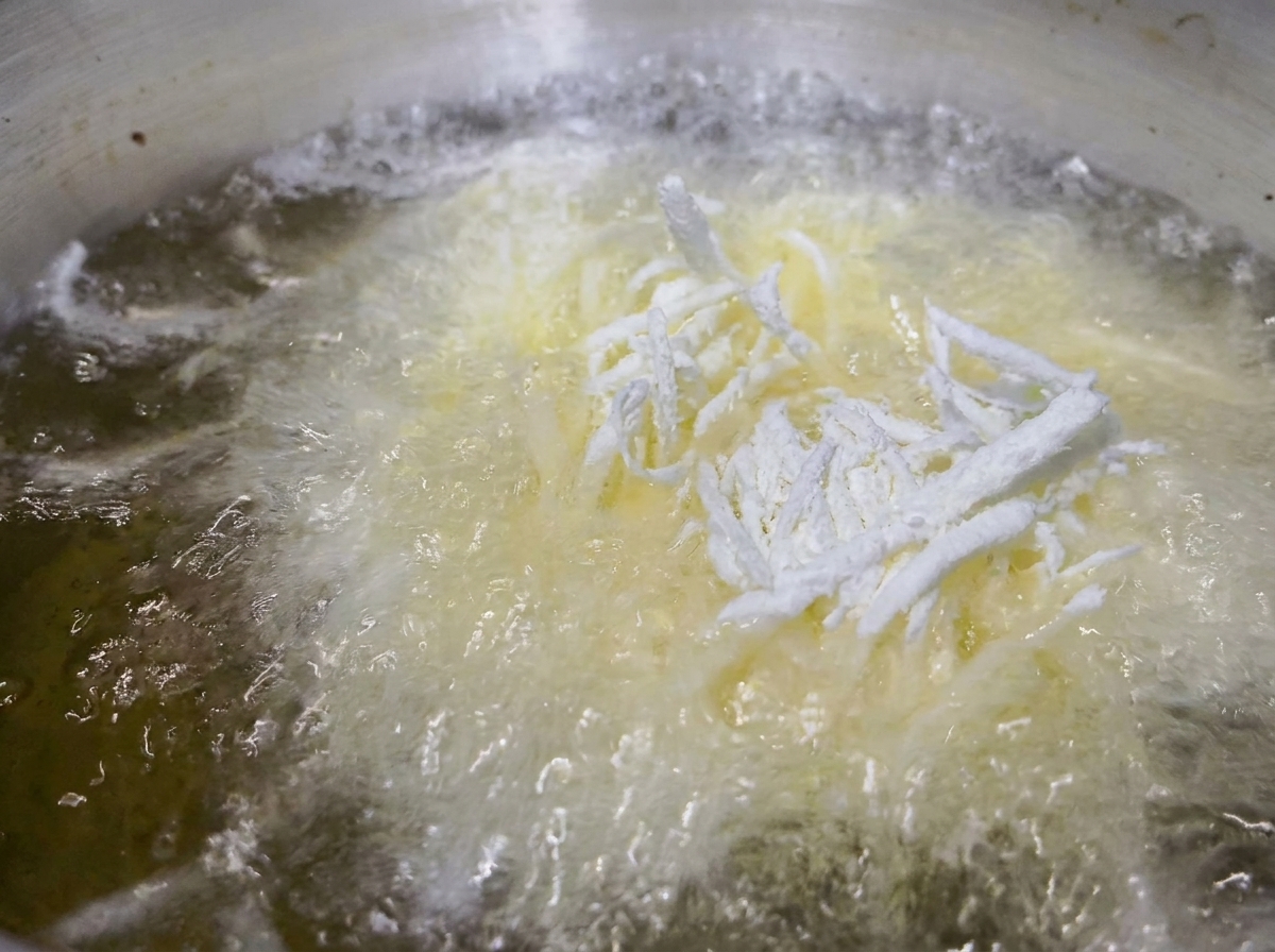 Tiras de papa enharinadas friéndose en una olla con aceite caliente burbujeante.