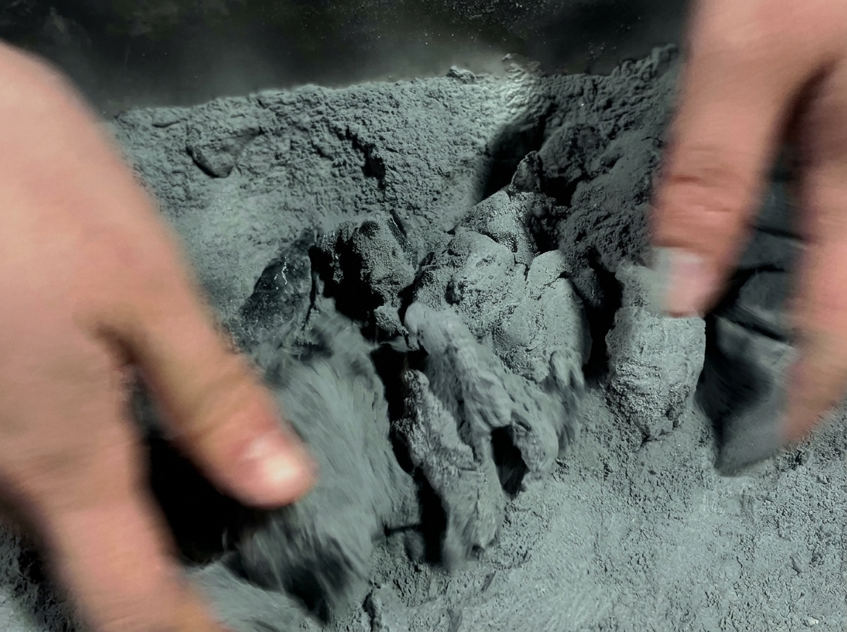 Manos frotando piezas de pollo marinado en una mezcla de polvo gris oscuro dentro de un contenedor.
