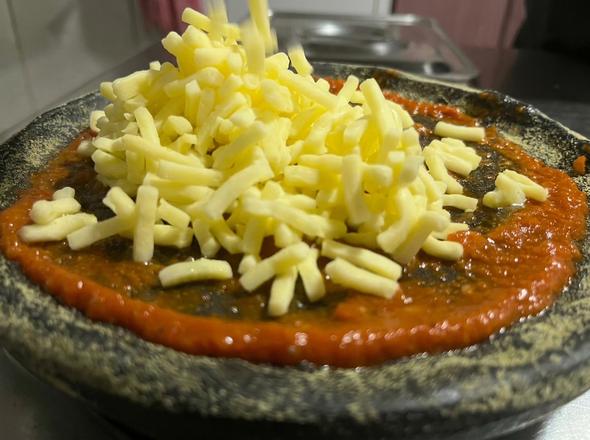 Primer plano de queso rallado cayendo sobre una capa de salsa de tomate roja en una masa de pizza de carbón.